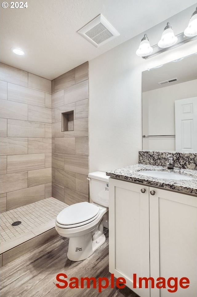 bathroom featuring vanity, toilet, wood-type flooring, and tiled shower