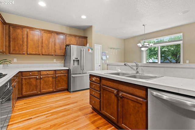 kitchen with light hardwood / wood-style flooring, hanging light fixtures, sink, an inviting chandelier, and stainless steel appliances