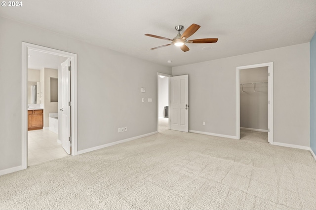 unfurnished bedroom featuring a walk in closet, ceiling fan, connected bathroom, and light colored carpet