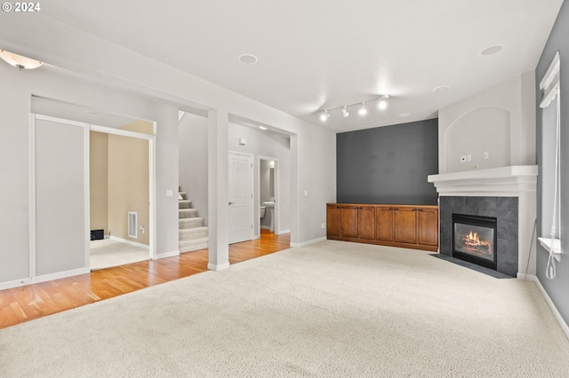 unfurnished living room featuring a tiled fireplace, rail lighting, and light wood-type flooring