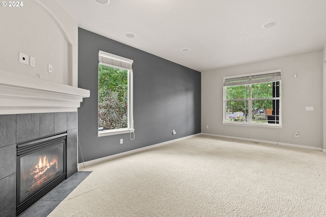 unfurnished living room featuring plenty of natural light, a tiled fireplace, and light carpet