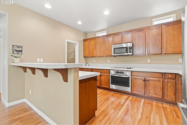 kitchen with a kitchen bar, appliances with stainless steel finishes, and light hardwood / wood-style floors