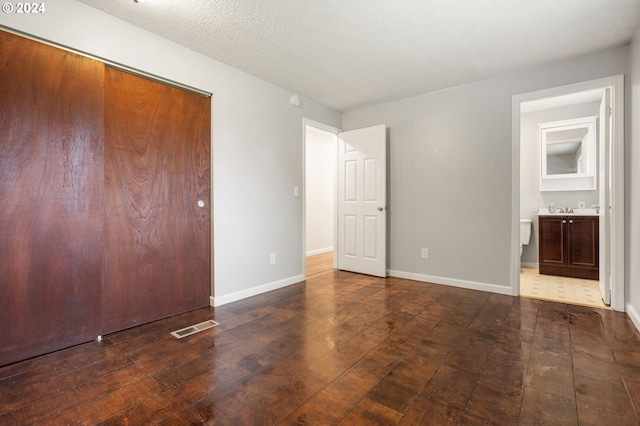 unfurnished bedroom with a closet, ensuite bath, dark hardwood / wood-style floors, and a textured ceiling