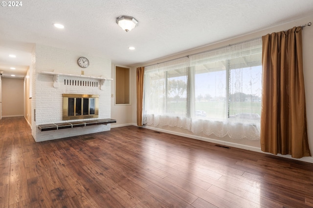 unfurnished living room with a brick fireplace, dark hardwood / wood-style floors, and a textured ceiling