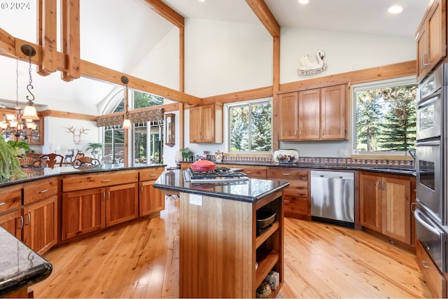 kitchen with dark stone countertops, stainless steel appliances, a center island, decorative light fixtures, and light wood-type flooring