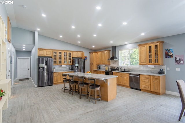 kitchen featuring lofted ceiling, a kitchen island, wall chimney exhaust hood, a kitchen breakfast bar, and stainless steel appliances