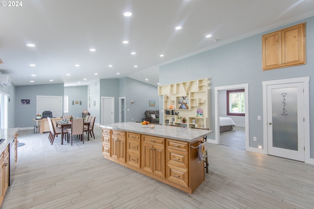 kitchen with light stone countertops, a center island, a wall unit AC, crown molding, and light hardwood / wood-style flooring