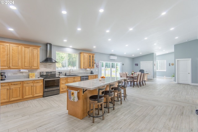 kitchen featuring wall chimney range hood, a breakfast bar area, sink, a center island, and appliances with stainless steel finishes