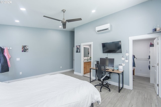 bedroom featuring a wall mounted air conditioner, light hardwood / wood-style flooring, ensuite bath, and ceiling fan