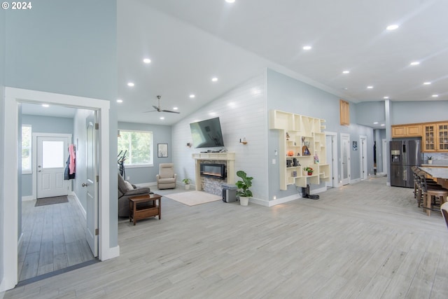 living room featuring a stone fireplace, high vaulted ceiling, light wood-type flooring, and ceiling fan