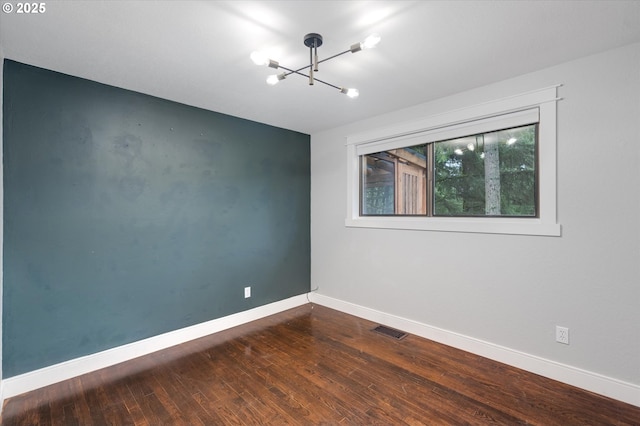 empty room with hardwood / wood-style flooring and an inviting chandelier