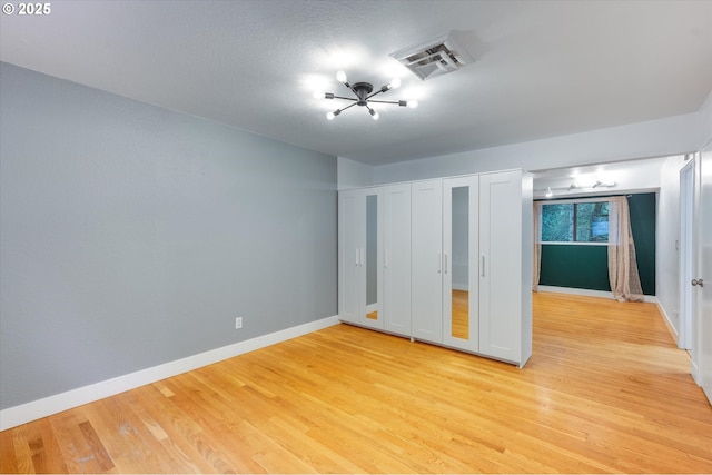 unfurnished bedroom with multiple closets, light hardwood / wood-style flooring, and a notable chandelier