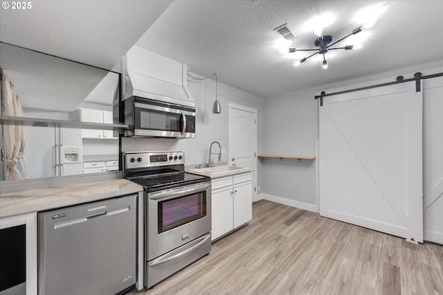 kitchen with appliances with stainless steel finishes, sink, a barn door, light hardwood / wood-style floors, and white cabinetry