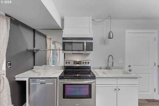 kitchen with light stone countertops, appliances with stainless steel finishes, sink, hardwood / wood-style flooring, and white cabinets