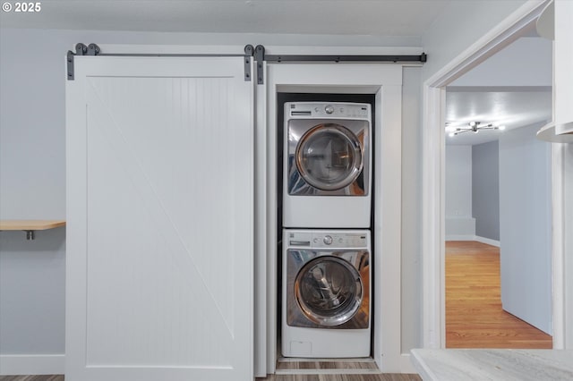 laundry room with a barn door, stacked washing maching and dryer, and hardwood / wood-style flooring