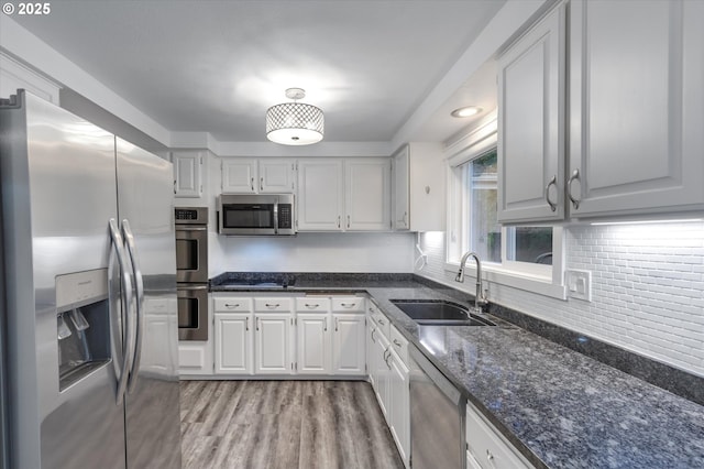 kitchen featuring sink, stainless steel appliances, dark stone countertops, white cabinets, and light wood-type flooring