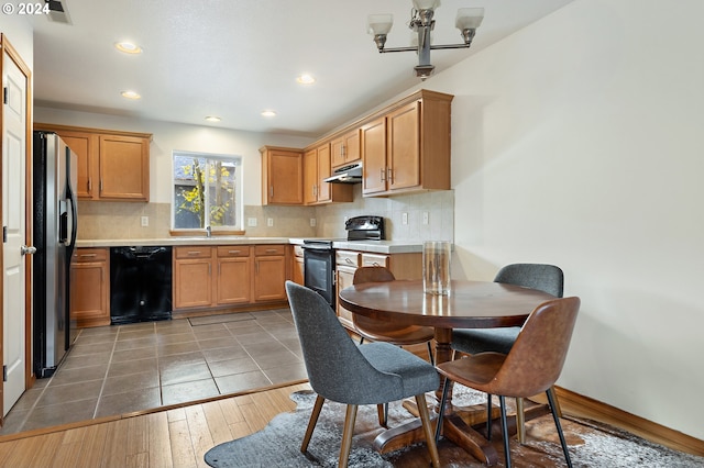 kitchen with dark wood-type flooring, an inviting chandelier, black appliances, sink, and tasteful backsplash