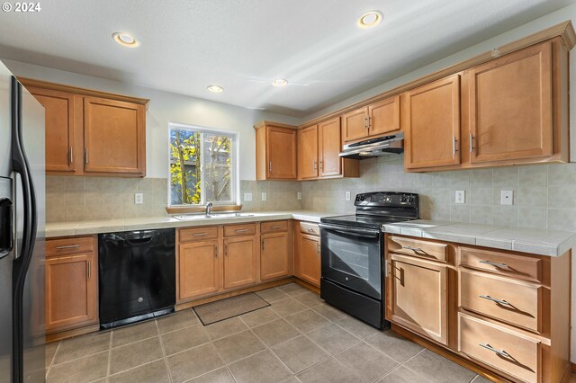 kitchen with sink, backsplash, dark tile patterned floors, and black appliances