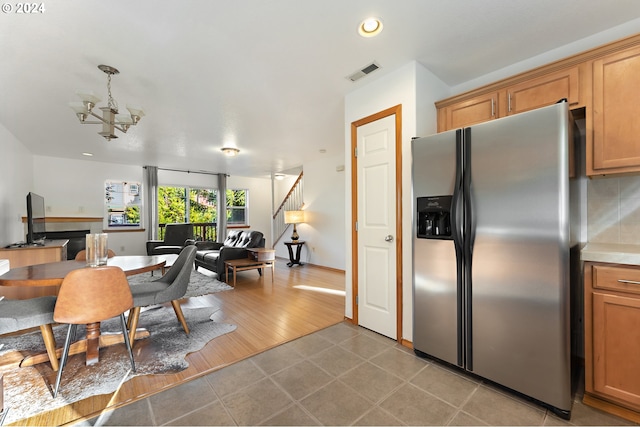 kitchen featuring pendant lighting, light hardwood / wood-style flooring, stainless steel fridge, a fireplace, and a notable chandelier