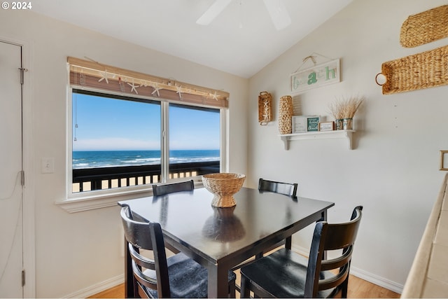 dining room featuring ceiling fan, a beach view, light hardwood / wood-style flooring, vaulted ceiling, and a water view