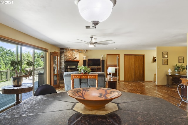 living room featuring wood-type flooring, a stone fireplace, and ceiling fan