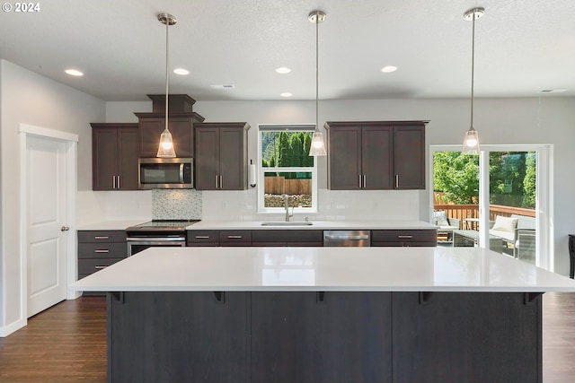 kitchen featuring appliances with stainless steel finishes, a kitchen bar, dark wood-type flooring, and pendant lighting