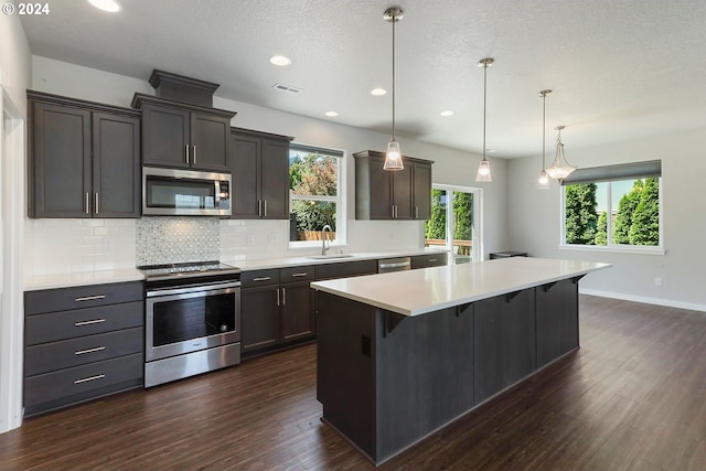 kitchen with dark wood-type flooring, pendant lighting, stainless steel appliances, and a textured ceiling