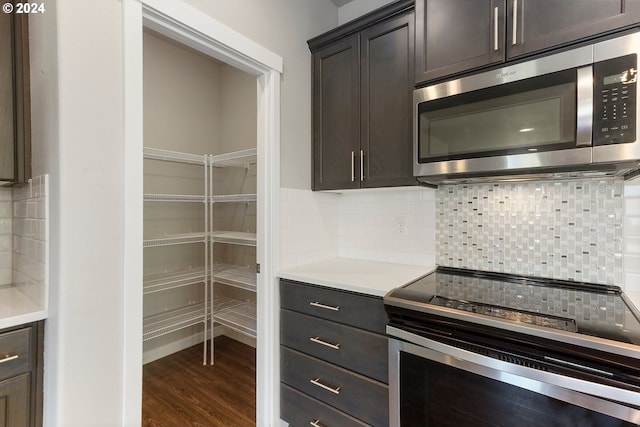 interior space featuring wood-type flooring, backsplash, dark brown cabinetry, and appliances with stainless steel finishes