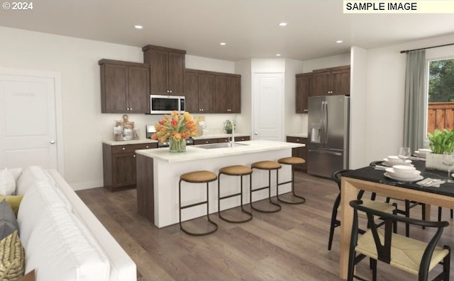 kitchen with wood finished floors, a sink, light countertops, a kitchen breakfast bar, and stainless steel fridge