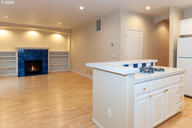 kitchen with white cabinetry, light hardwood / wood-style flooring, white refrigerator, a tiled fireplace, and a kitchen island