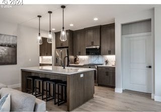 kitchen with appliances with stainless steel finishes, dark brown cabinets, sink, hanging light fixtures, and an island with sink