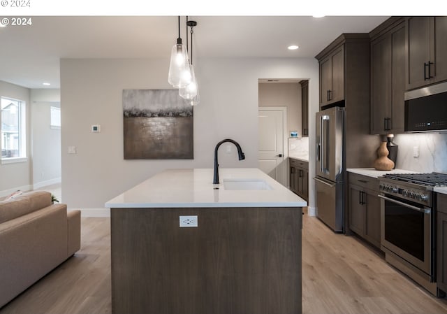 kitchen with high end appliances, a kitchen island with sink, decorative light fixtures, light hardwood / wood-style floors, and dark brown cabinetry