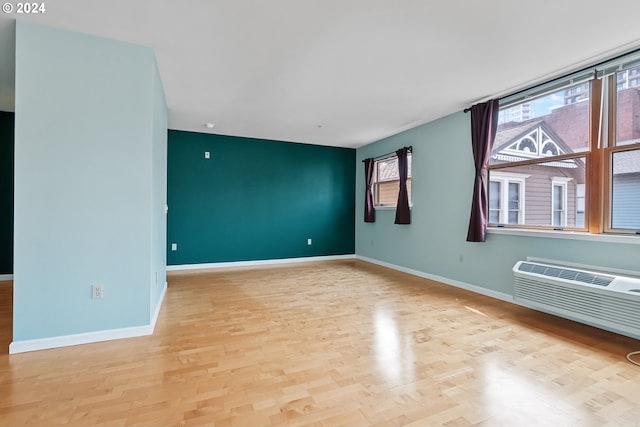 unfurnished room featuring a wall mounted AC, wood finished floors, and baseboards