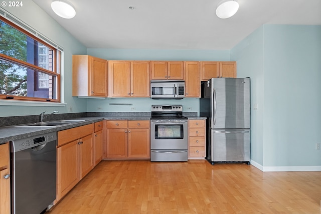 kitchen with light wood-type flooring, dark countertops, stainless steel appliances, and a sink