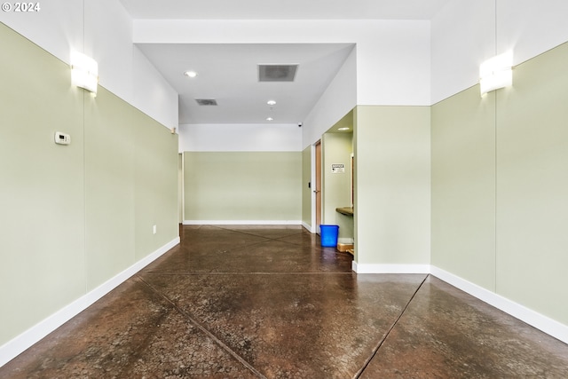 hall featuring concrete flooring, visible vents, and baseboards