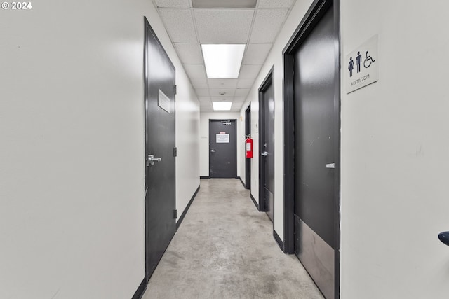 corridor with concrete floors, a drop ceiling, and baseboards