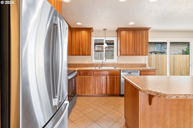 kitchen featuring pendant lighting, sink, a textured ceiling, light tile patterned flooring, and stainless steel appliances