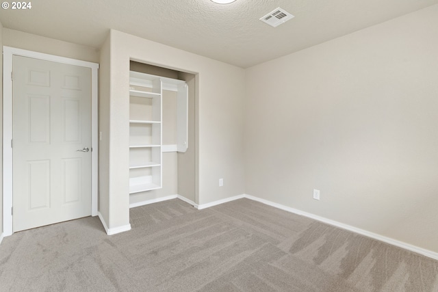 unfurnished bedroom featuring light colored carpet, a textured ceiling, and a closet