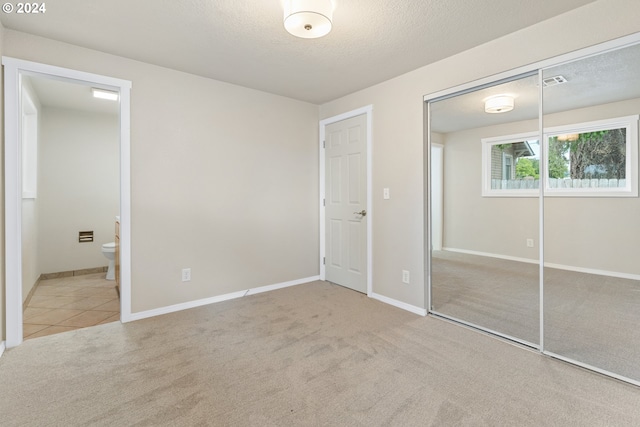 unfurnished bedroom with light carpet, a textured ceiling, a closet, and connected bathroom