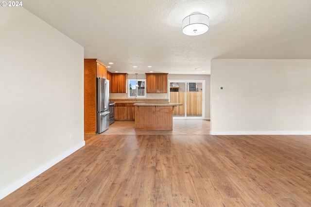 kitchen featuring stainless steel refrigerator, a center island, a textured ceiling, a breakfast bar, and light wood-type flooring