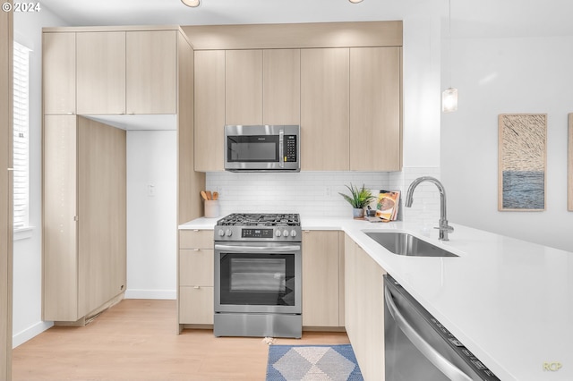 kitchen with decorative light fixtures, stainless steel appliances, light hardwood / wood-style floors, sink, and backsplash