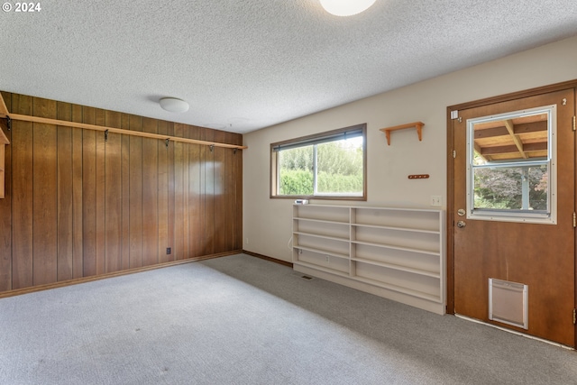 spare room featuring wooden walls, light colored carpet, and a textured ceiling