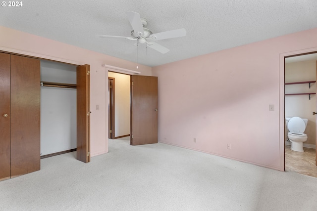 unfurnished bedroom featuring light carpet, ceiling fan, a textured ceiling, ensuite bathroom, and a closet