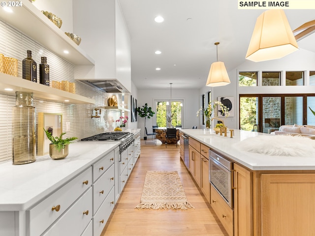 kitchen featuring white cabinets, hanging light fixtures, appliances with stainless steel finishes, a spacious island, and light hardwood / wood-style floors