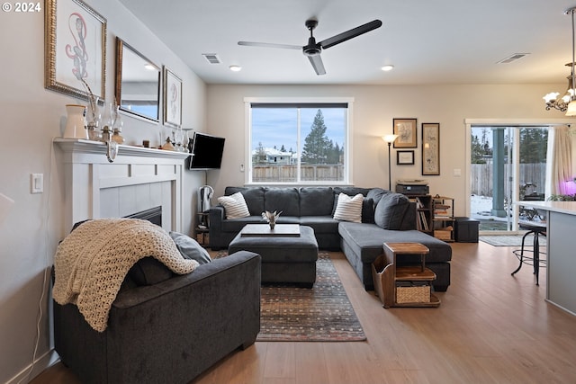 living room featuring a fireplace, a healthy amount of sunlight, ceiling fan with notable chandelier, and light hardwood / wood-style floors