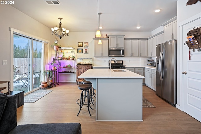 kitchen with appliances with stainless steel finishes, decorative light fixtures, light hardwood / wood-style floors, and an island with sink