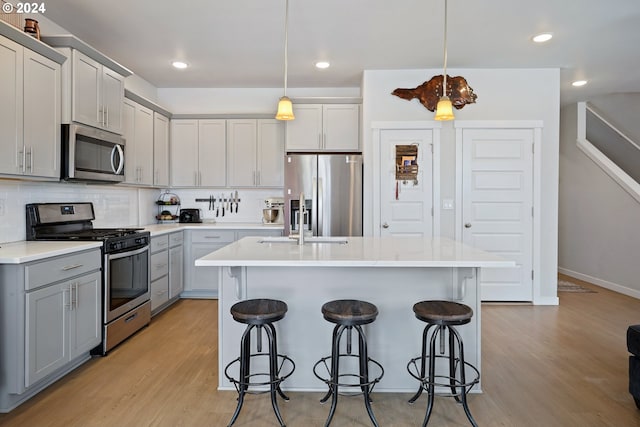 kitchen with pendant lighting, light hardwood / wood-style floors, a center island with sink, and stainless steel appliances