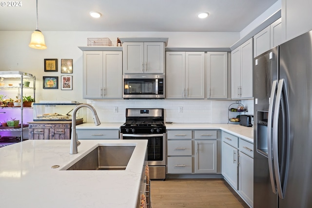 kitchen with sink, hanging light fixtures, gray cabinets, light wood-type flooring, and stainless steel appliances