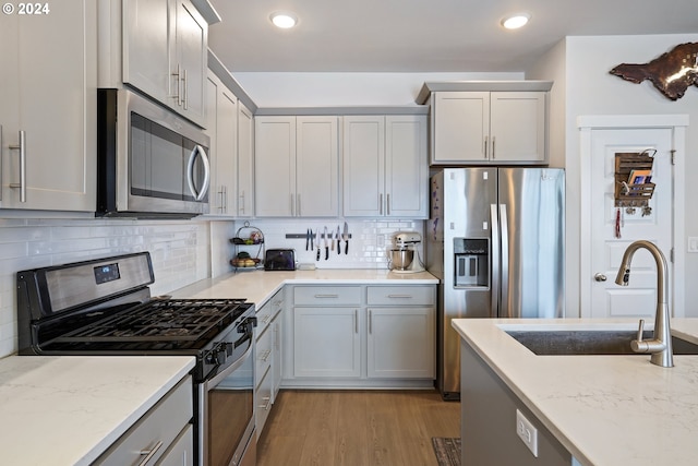 kitchen with light wood-type flooring, tasteful backsplash, gray cabinetry, stainless steel appliances, and sink