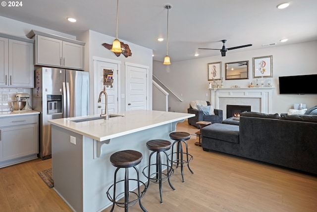 kitchen featuring gray cabinetry, sink, hanging light fixtures, an island with sink, and light wood-type flooring